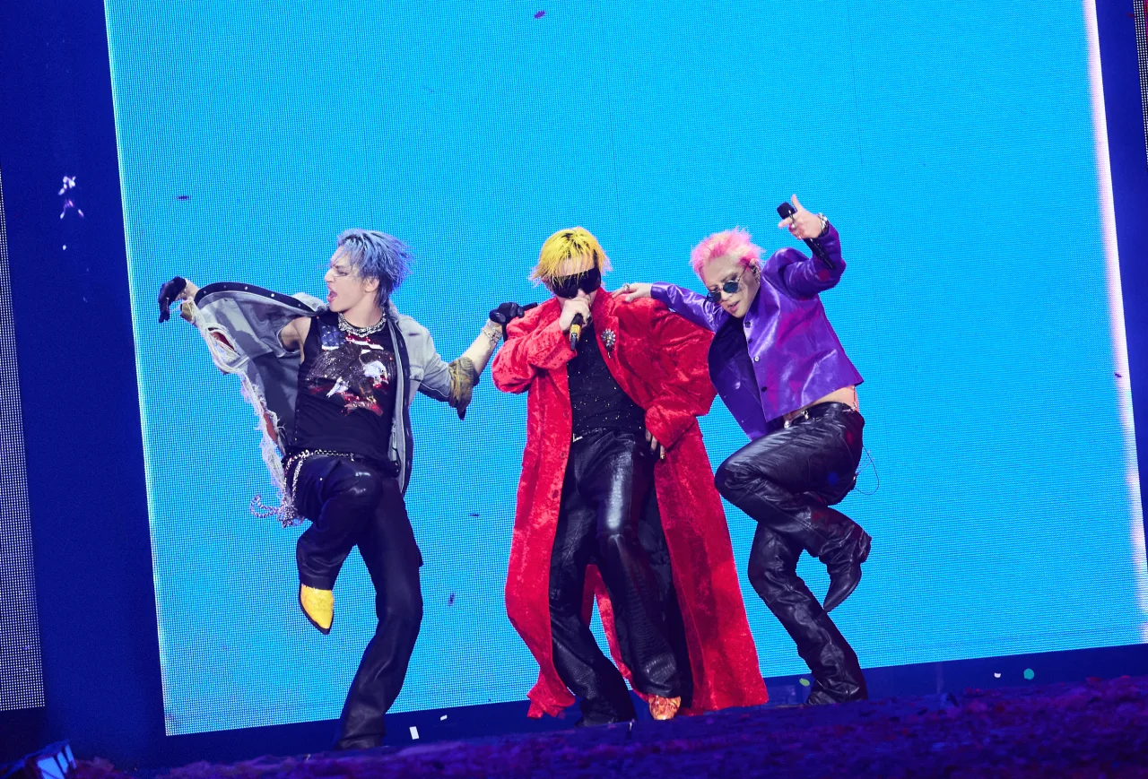 Jovem suando, usando fones, faz polichinelos ao som de ‘Fantastic Baby’ com cartaz do BIGBANG ao fundo