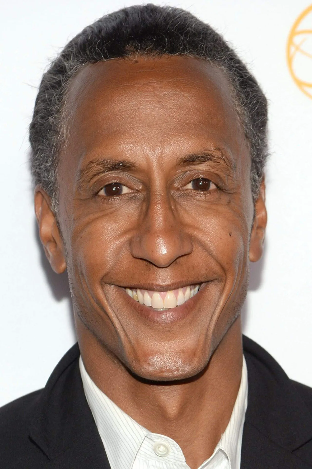 Andre Royo levanta halteres de ferro em uma academia, com uma coqueteleira e toalha sobre o banco de musculação