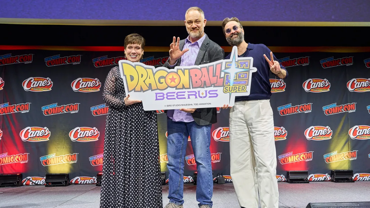 Beerus e Goku posam diante de um grande banner de Dragon Ball no palco iluminado do NYCC 2026