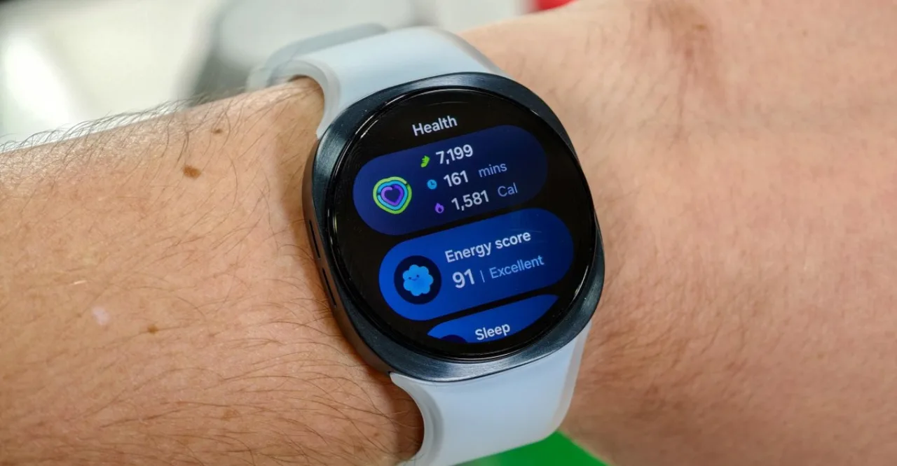 Galaxy Watch 9 no pulso de atleta, ao lado de halteres de ferro e garrafa de água, destacando a tela vibrante