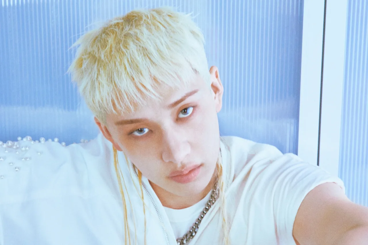 Bang Chan sorrindo ao lado de um bolo de aniversário, segurando um envelope com 300 mi won e o logo da JYP