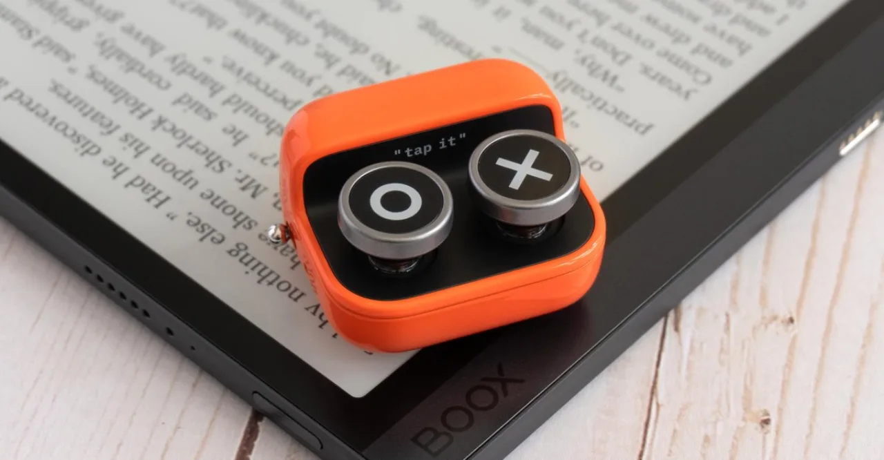 Pessoa usando controle retro estilo fidget ao lado de e‑reader, com garrafa d'água e tapete de yoga