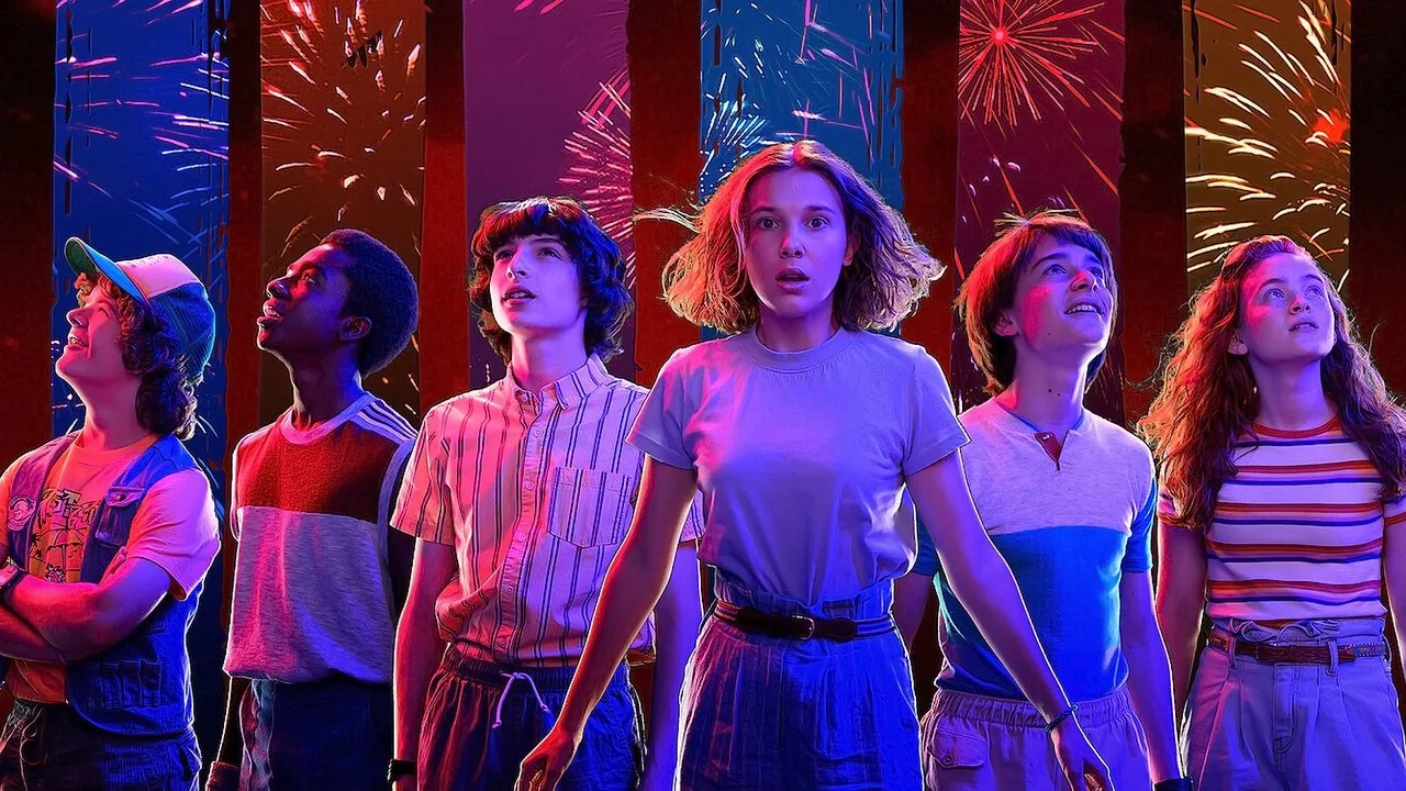 Jovem malhando com halteres, garrafa de água e laptop exibindo o trailer de Stranger Things na tela