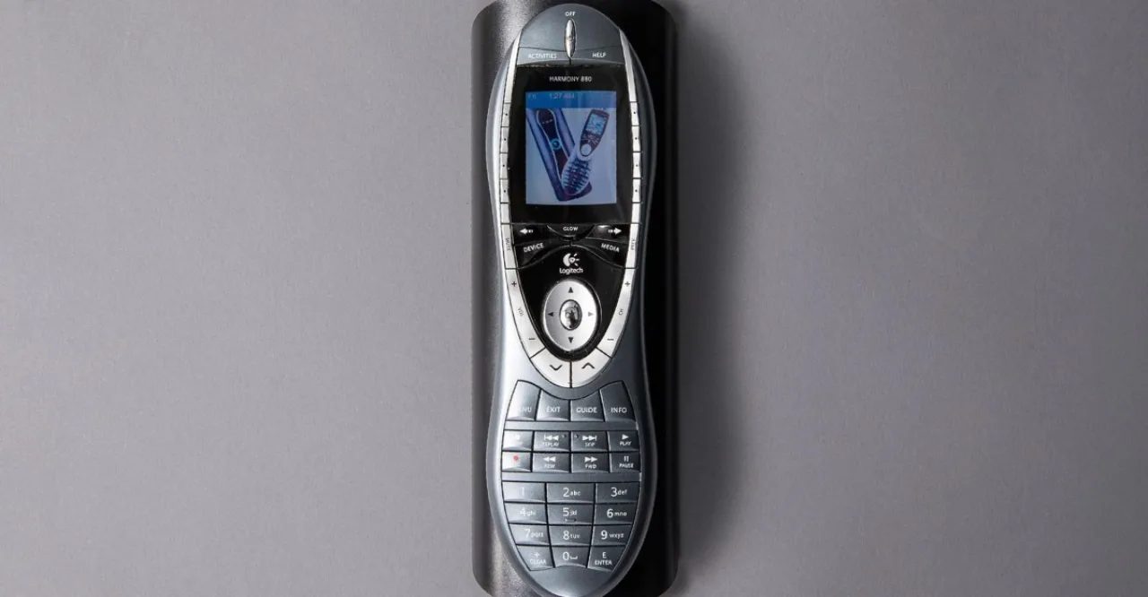 Pessoa em roupa de treino segurando o controle remoto Logitech Harmony ao lado de um tapete de yoga