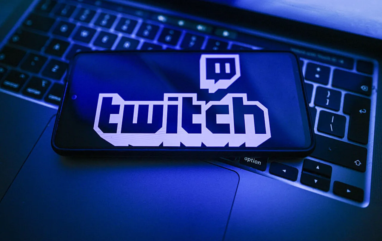 Um gamer em frente ao monitor, com fone, garrafa de água e halteres ao lado, demonstrando foco e bem‑estar enquanto transmite