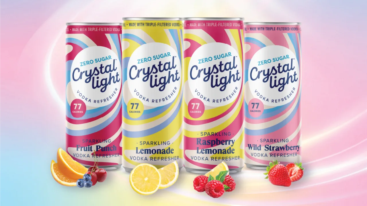Taça de vidro com drink colorido, gelo, fatias de limão e sachê de Crystal Light sobre uma mesa ensolarada
