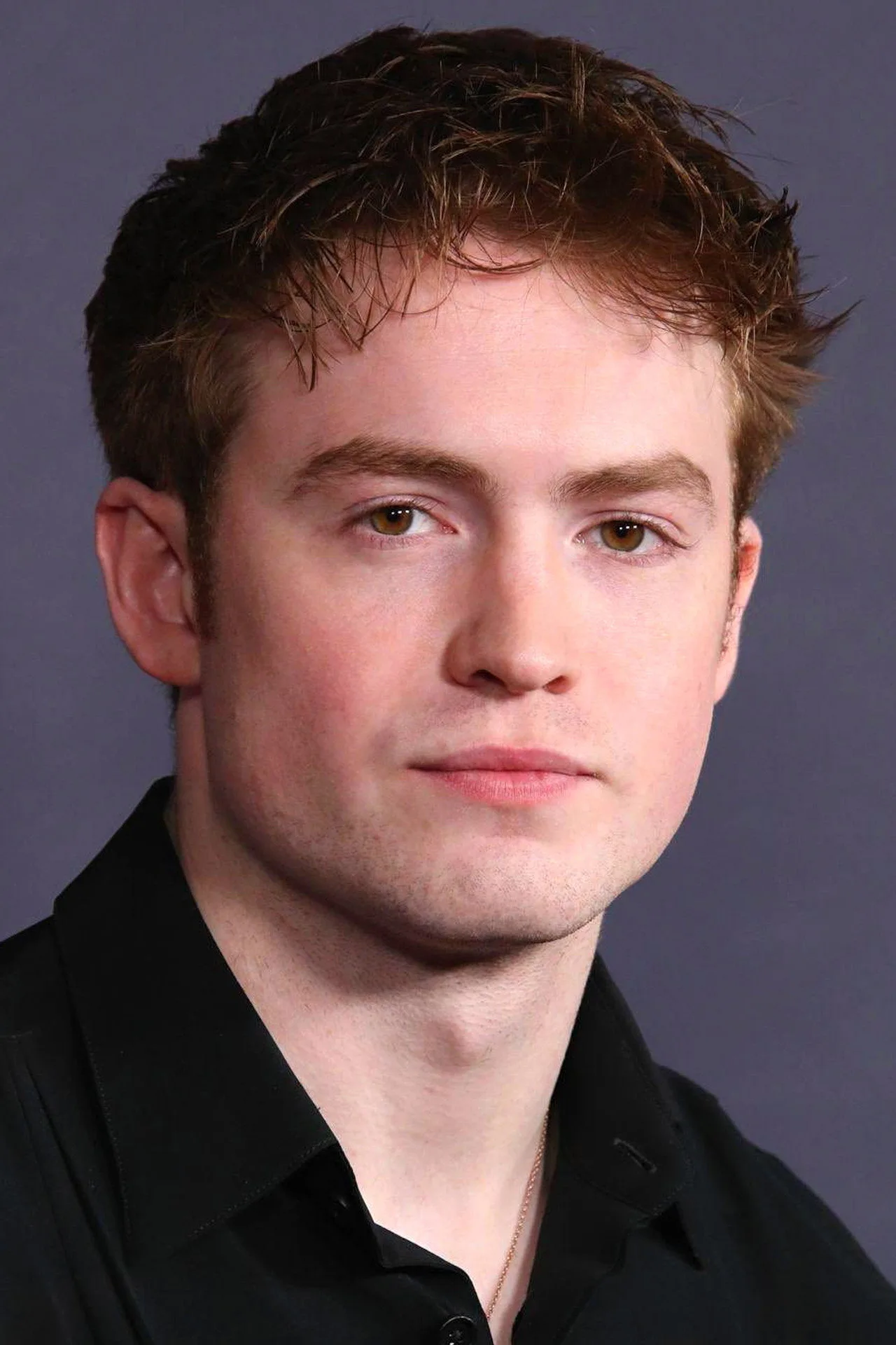 Kit Connor sem camisa empurrando halteres pesados, ombros largos e abdômen trincado à mostra