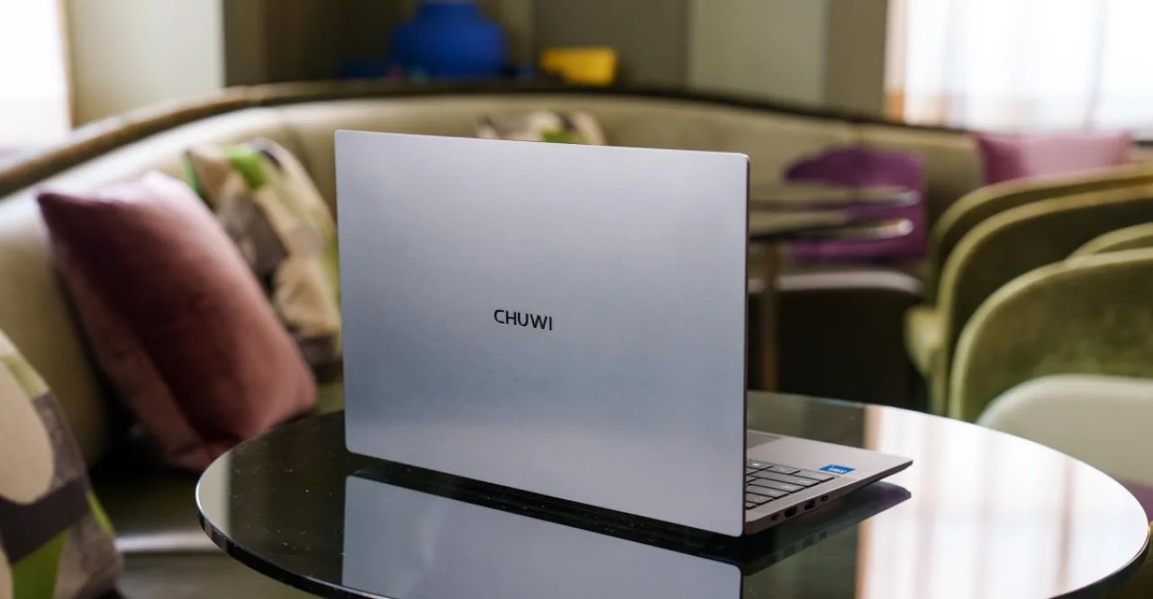 Jovem sentado em cadeira ergonômica, laptop aberto ao lado de halteres e garrafa de água