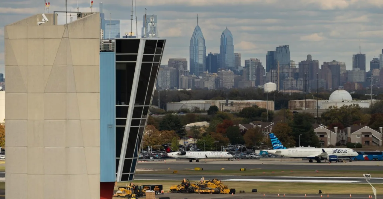 Cabos de fibra óptica expostos ao lado de uma escavadeira, com o logotipo da Verizon ao fundo e aviões aguardando