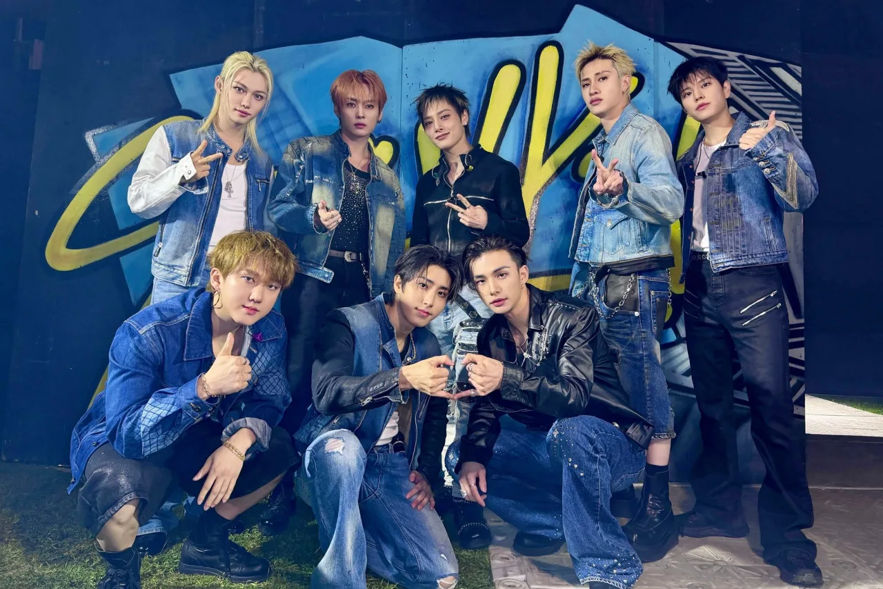 Membros do Stray Kids posam ao lado do disco ‘THIS & THAT’ com o logo da Billboard 200 destacando a posição 15