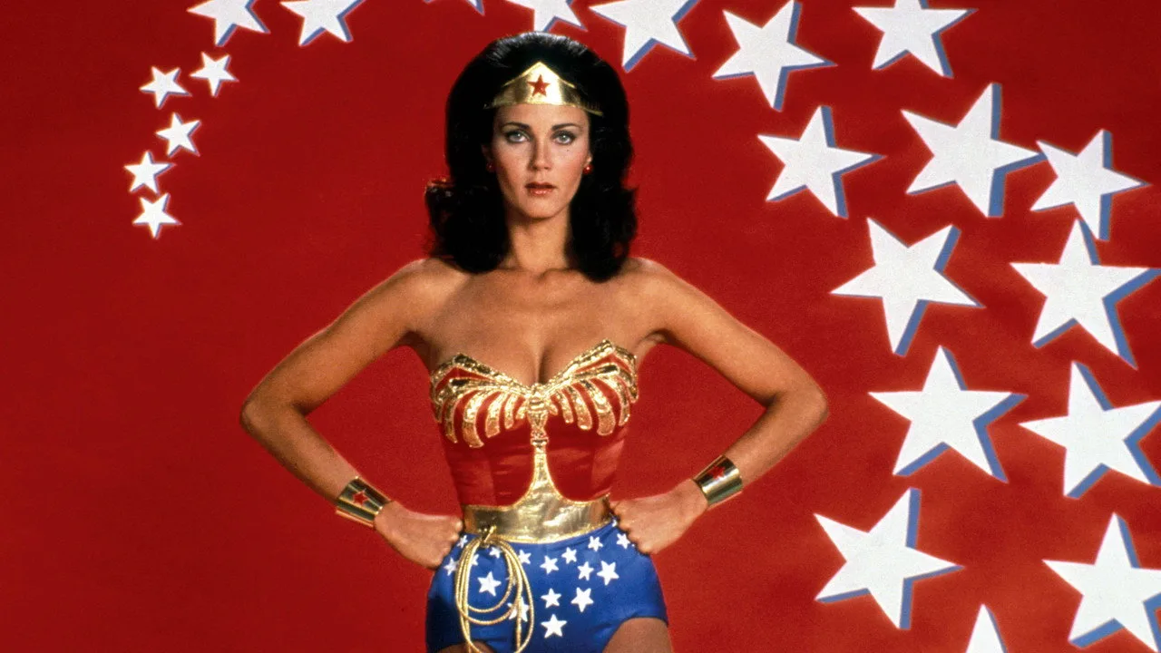 Mulher em roupa de treino azul, segurando halteres, ao fundo pôster da Wonder Woman
