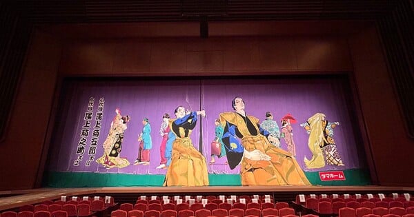Araki segurando lápis, esboçando cortinas coloridas, com o palco de Kabuki ao fundo iluminado